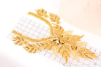 a close-up view of a gold-colored embroidered piece with intricate details, including leaves and flowers, placed on a white surface.