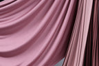 a close-up view of a flowing, draped fabric with a soft, pinkish hue. The fabric appears to be made of a smooth, shiny material, possibly silk or satin, and is draped in a way that creates a sense of movement and elegance. The fabric is draped over a surface, adding a touch of sophistication and style to the scene.