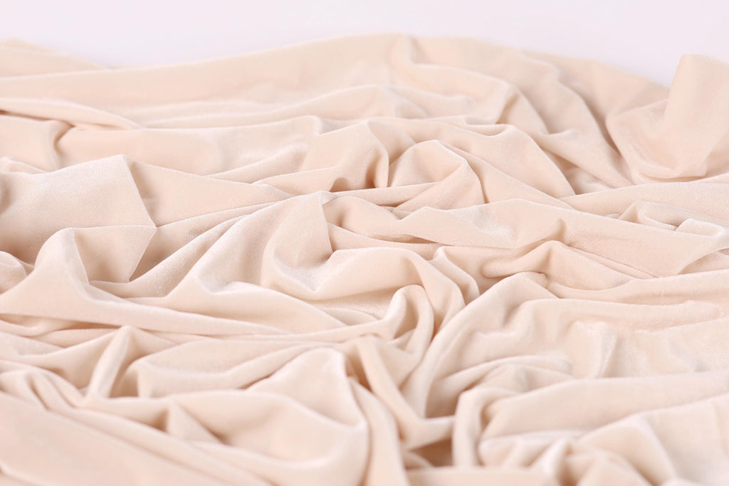 The image is a close-up of a crumpled, light pink fabric, possibly velvet, with a soft, wrinkled texture.