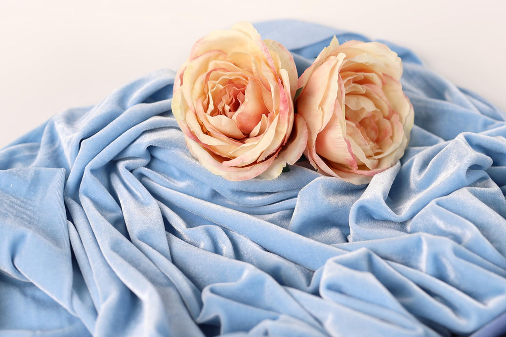 Two delicate pink roses resting on a crumpled blue fabric.