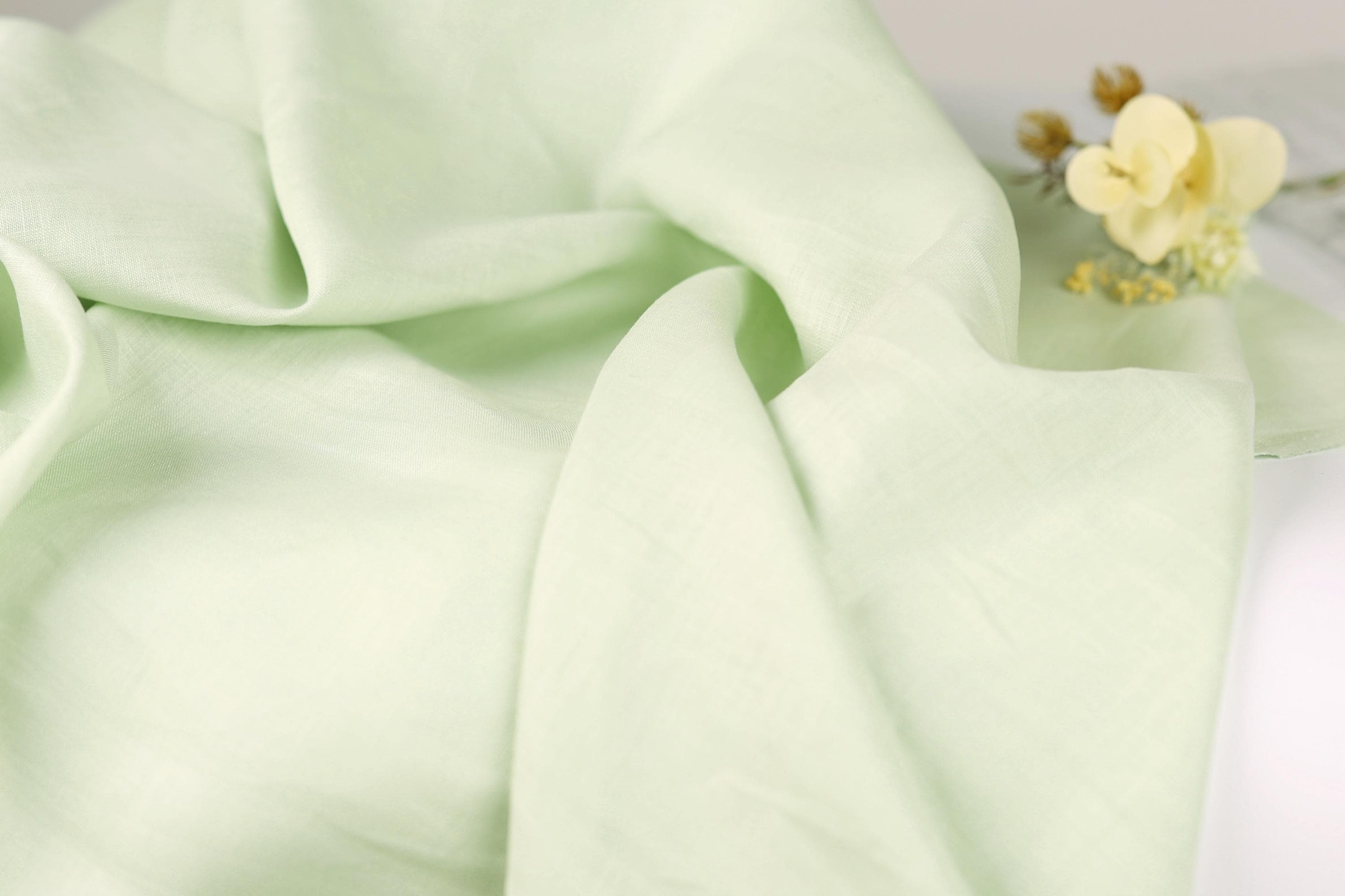 a close-up view of a light green fabric, with a small yellow flower resting on it.