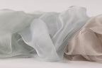 a close-up view of three different colored silks or fabrics, including a light blue, a light gray, and a light brown color.