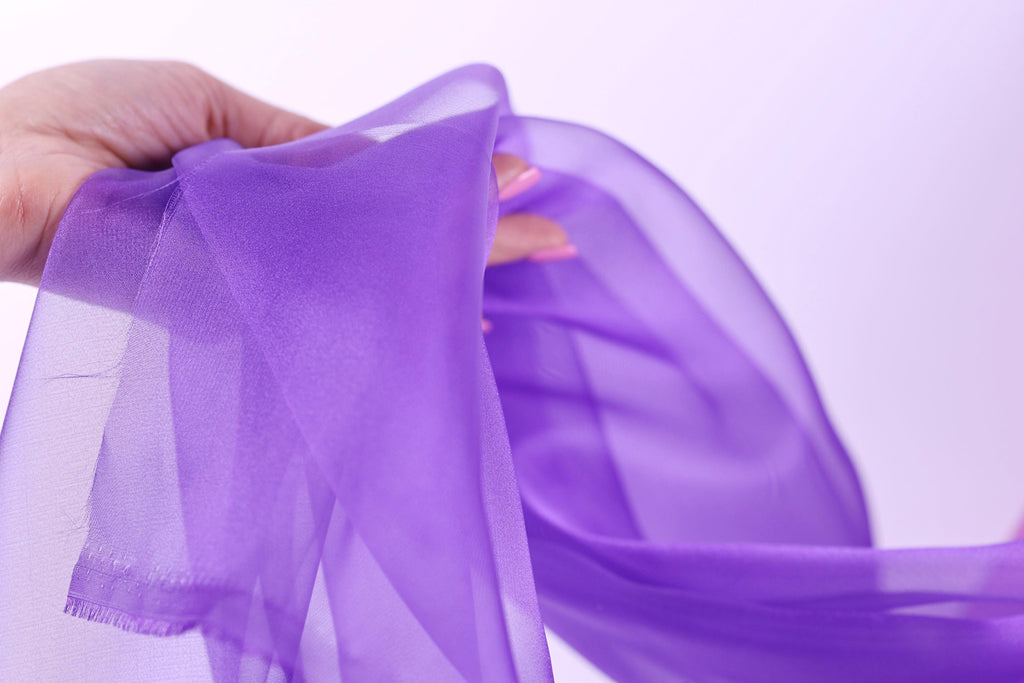 A hand is holding a purple fabric, which appears to be a scarf or garment.