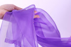 A hand is holding a purple fabric, which appears to be a scarf or garment.