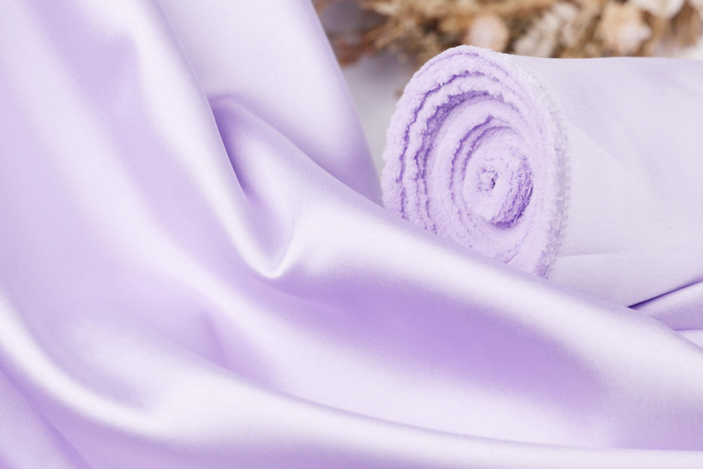A close-up view of a soft, flowing purple fabric, possibly silk or satin, with a curled edge visible.