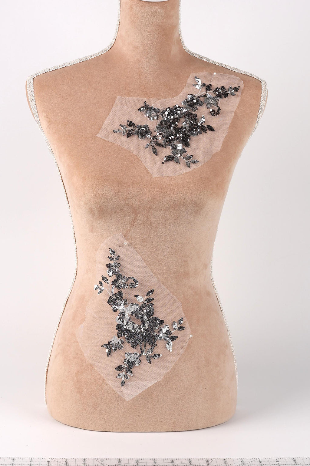 a mannequin torso with two pieces of fabric attached to it, one on each side. The fabric appears to be a decorative element, possibly a lace or a floral pattern, with small black and silver sequins or beads attached to it.