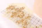 a close-up view of a piece of fabric with gold sequin flowers and leaves, placed on a transparent ruler.
