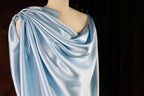 A mannequin wearing a blue satin draped over its shoulder, with a dark background.