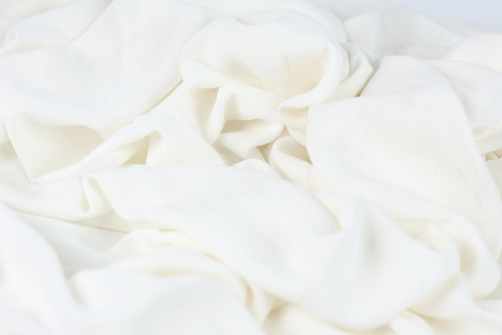 The image is a close-up of a white fabric, possibly a piece of clothing or a textile. The fabric appears to be crumpled and wrinkled, giving it a soft and delicate appearance.