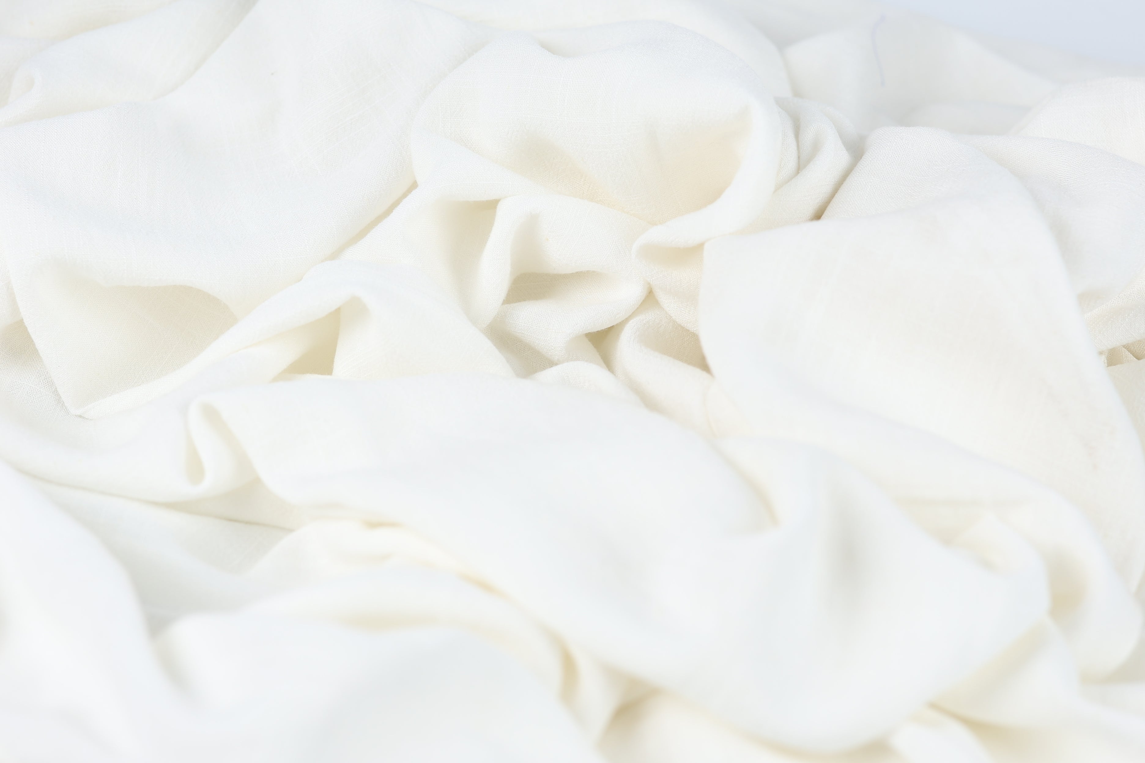 The image is a close-up of a white fabric, possibly a piece of clothing or a textile. The fabric appears to be crumpled and wrinkled, giving it a soft and delicate appearance.