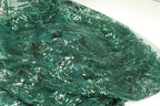a close-up view of a fabric with a green, sequined pattern. The fabric appears to be made of a shiny, green material with a floral or leaf-like design. The fabric is folded and crumpled, giving it a textured appearance.
