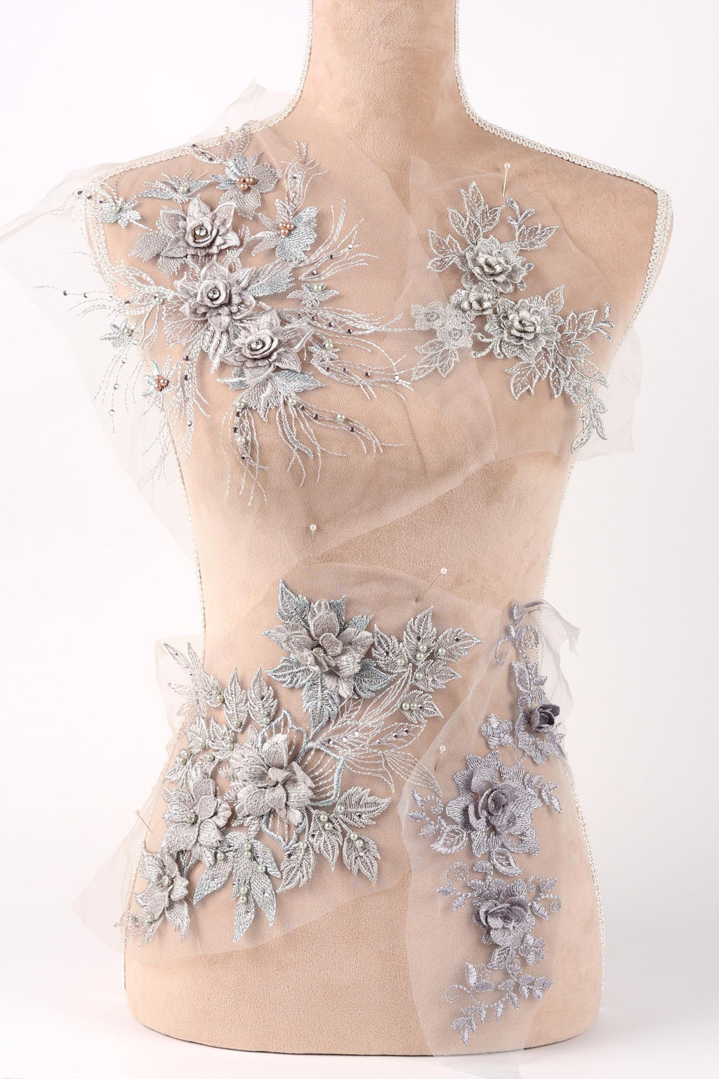 A mannequin torso with a beige fabric, adorned with intricate silver floral and leaf designs.