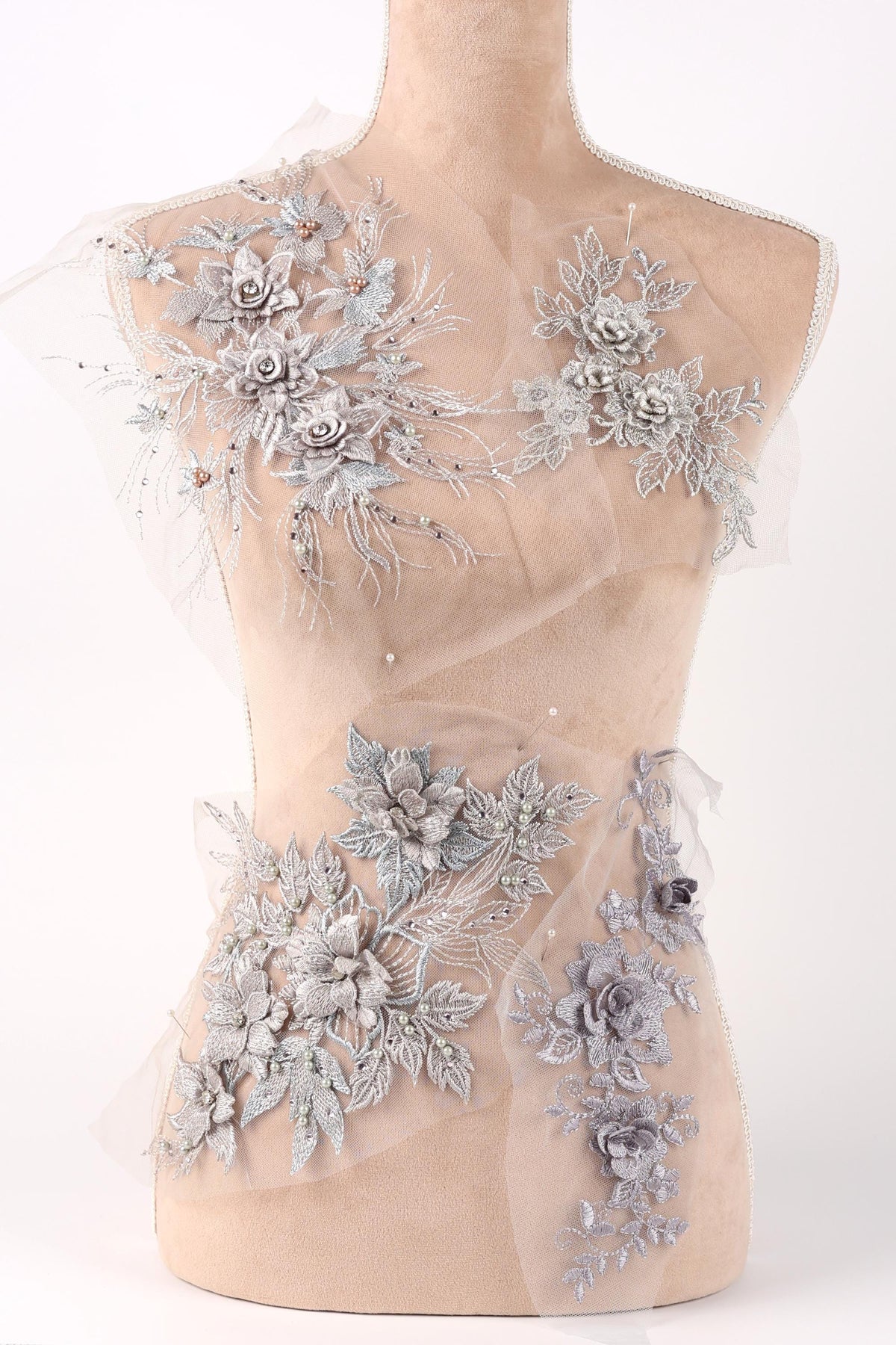 A mannequin torso with a beige fabric, adorned with intricate silver floral and leaf designs.