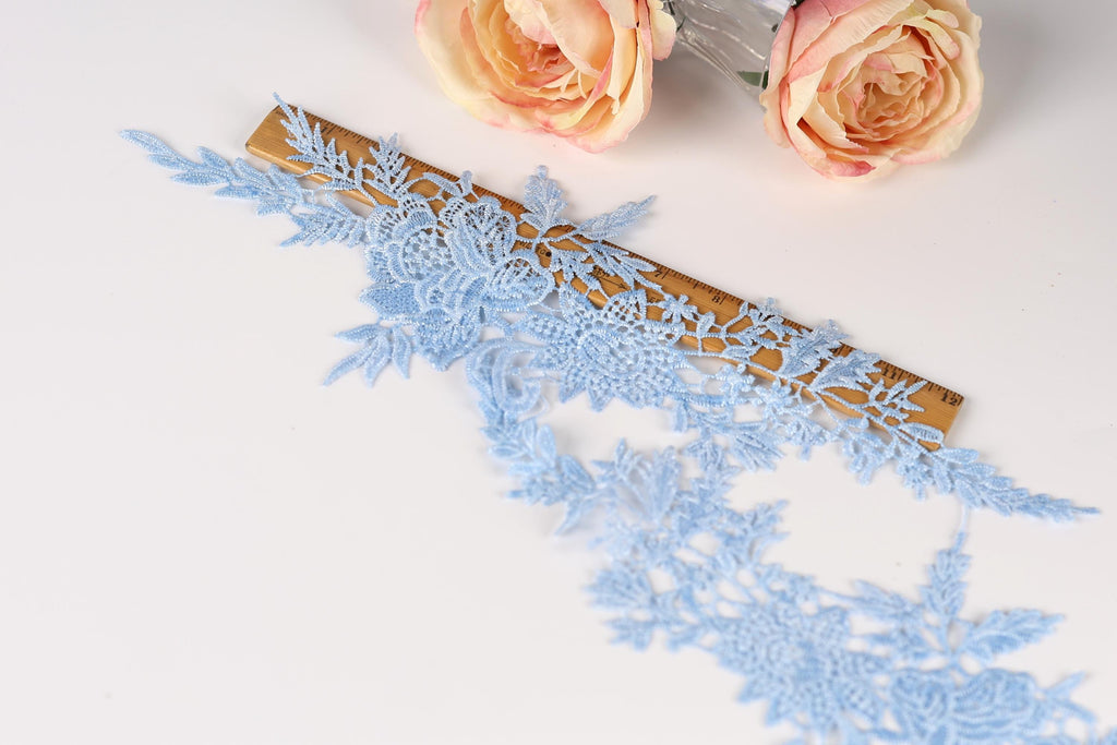 a close-up view of a delicate blue lace fabric with intricate floral patterns, placed next to a ruler on a white surface.