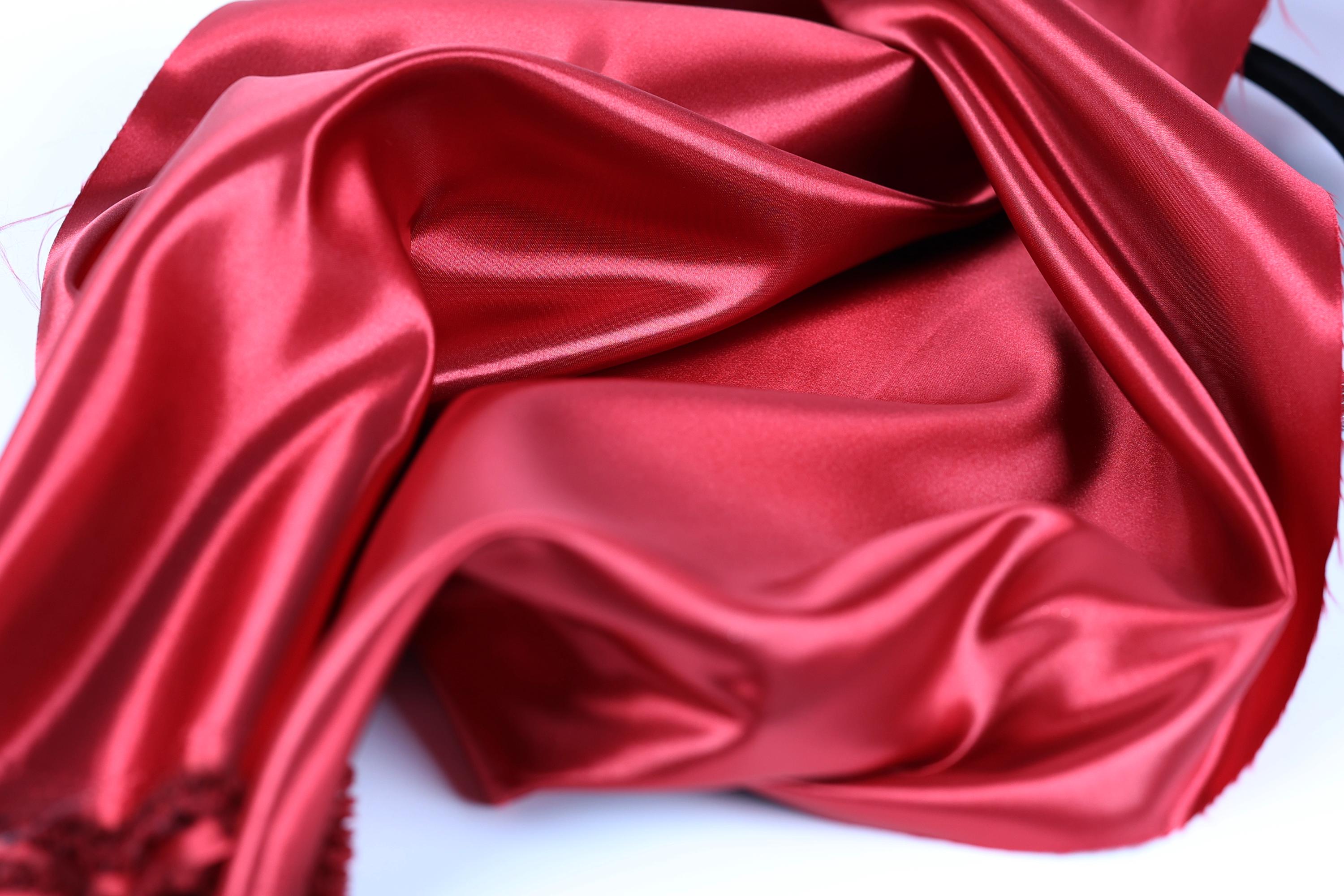 a close-up view of a red satin fabric, with its smooth and shiny texture visible.