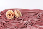 Two light pink roses resting on a crumpled pink fabric.