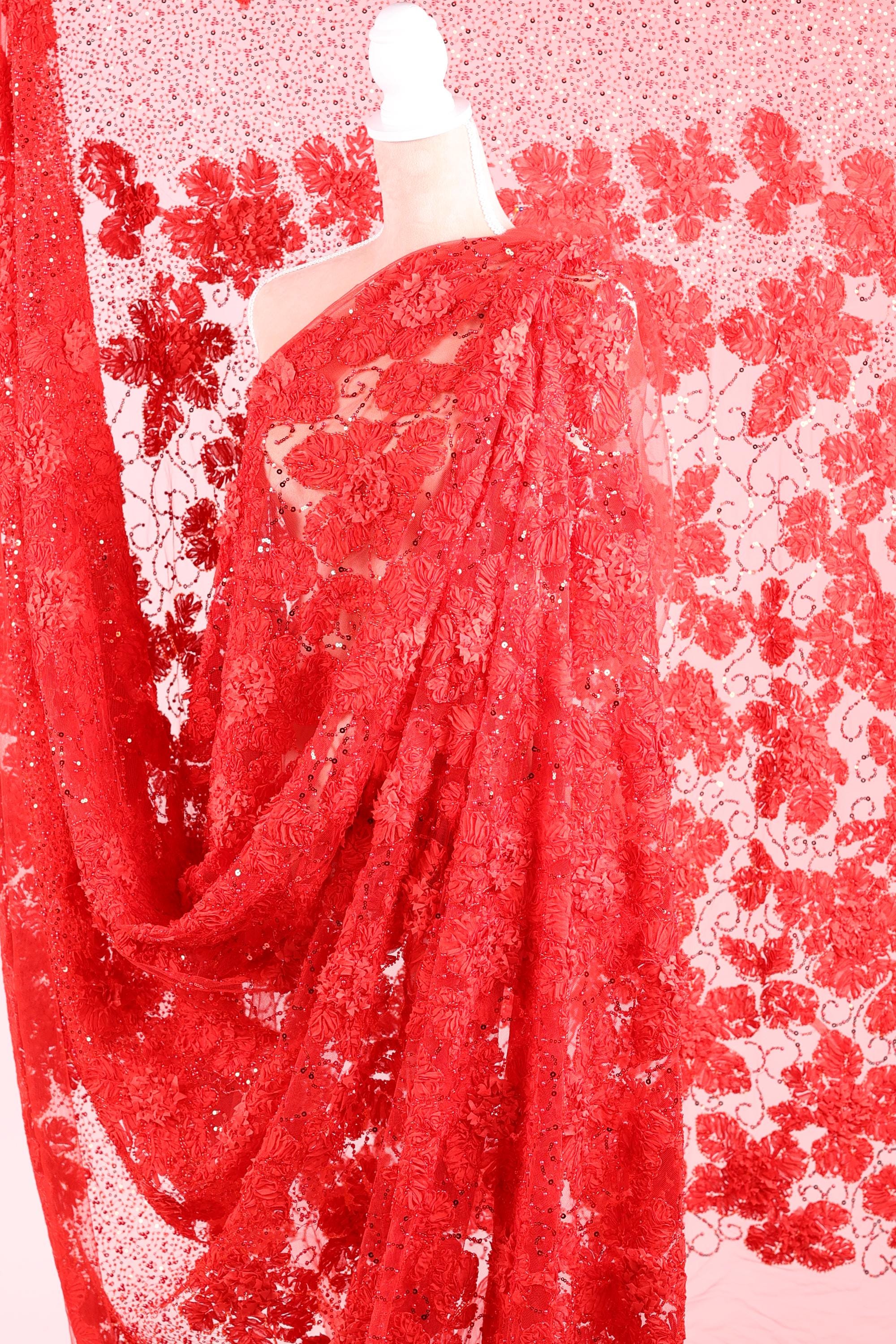 a close-up view of a red lace fabric with a floral pattern. The fabric appears to be made of a sheer material, giving it a delicate and elegant appearance. The lace fabric is spread out, creating a sense of movement and texture in the image.