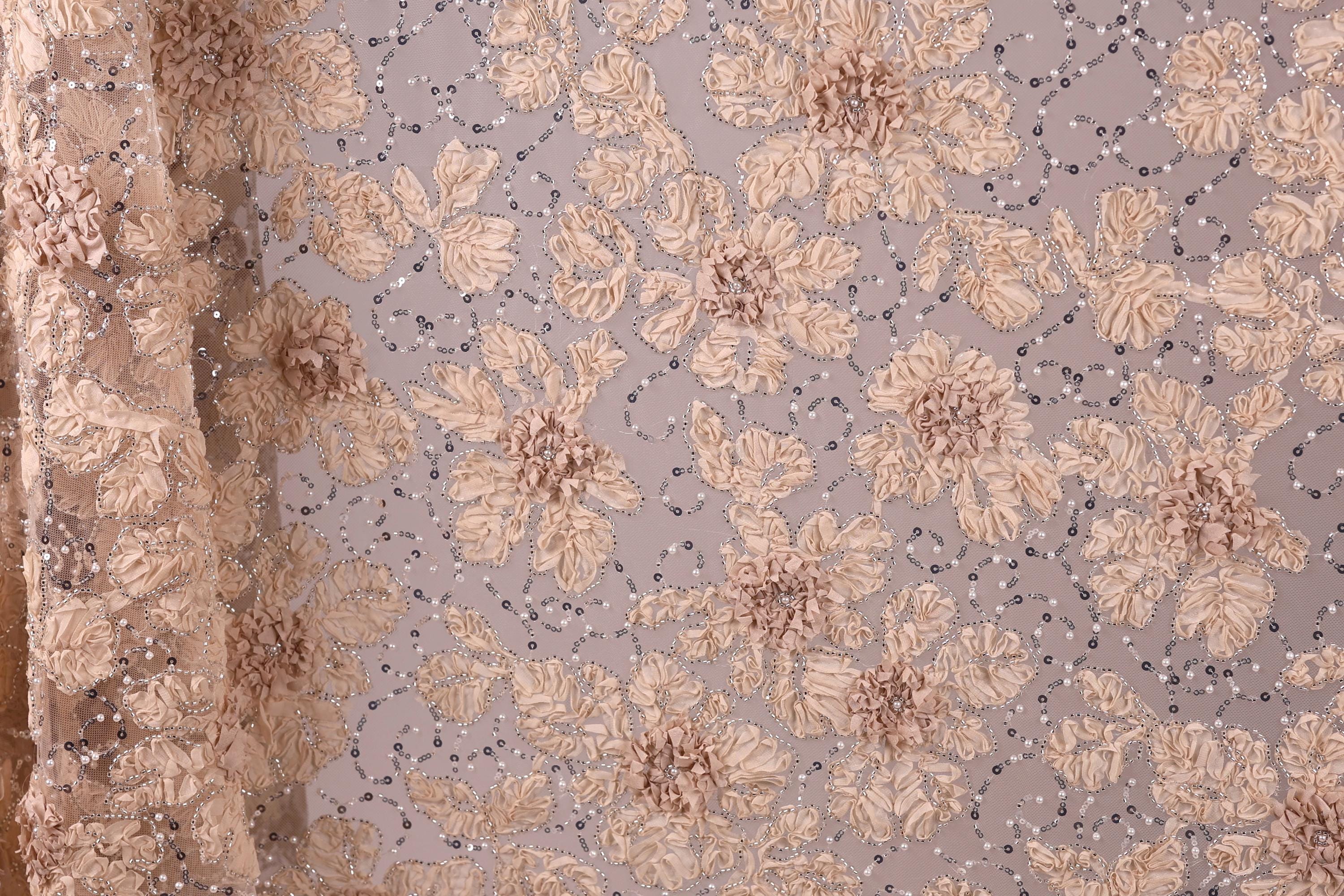a close-up view of a fabric with a floral pattern, including beige and brown flowers and small white beads or sequins.