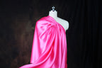 A mannequin wearing a bright pink satin dress with a draped, flowing silhouette.