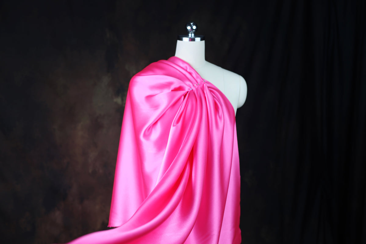 A mannequin wearing a bright pink satin dress with a draped, flowing silhouette.