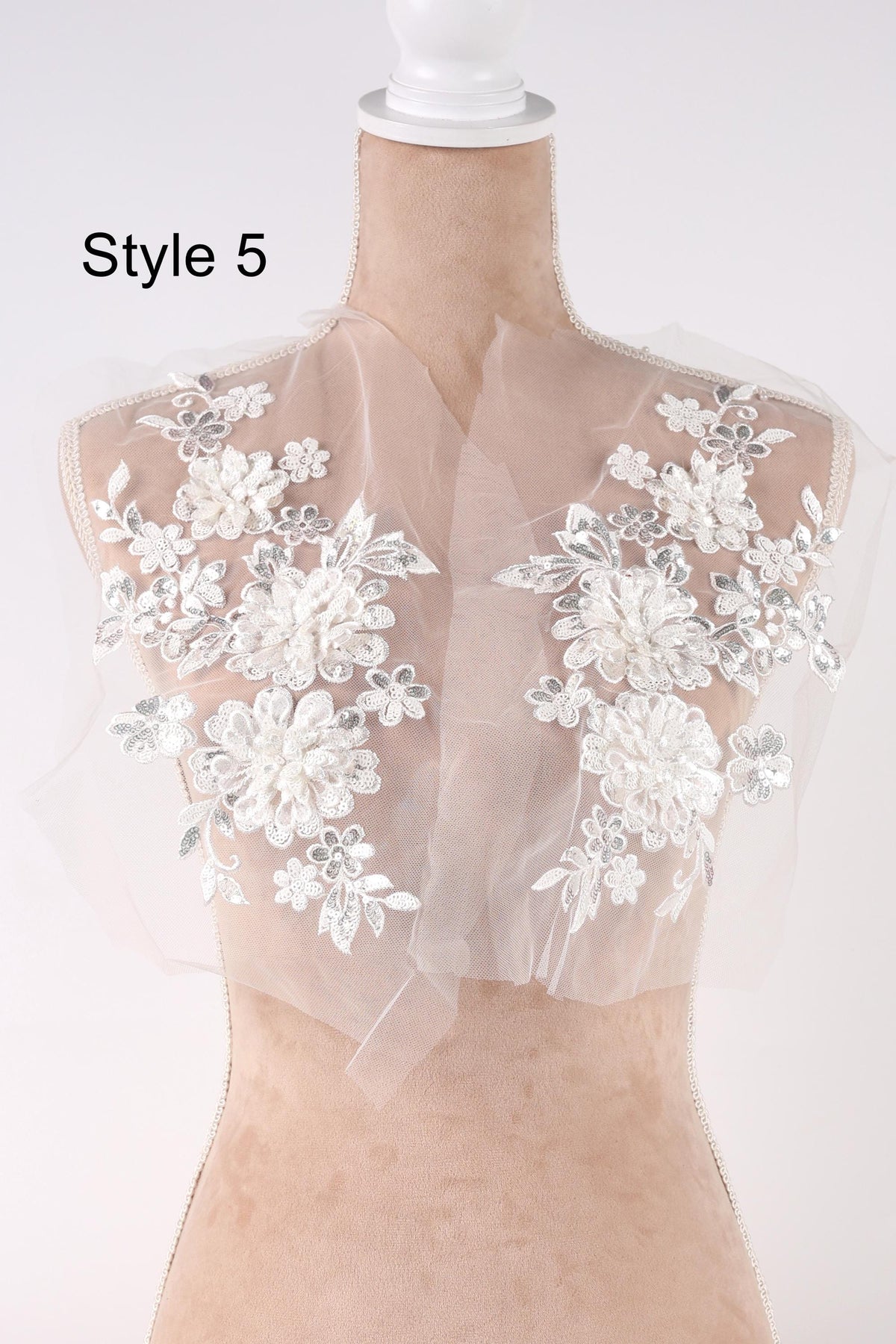A mannequin wearing a white lace dress with floral embroidery on the shoulders and neck.