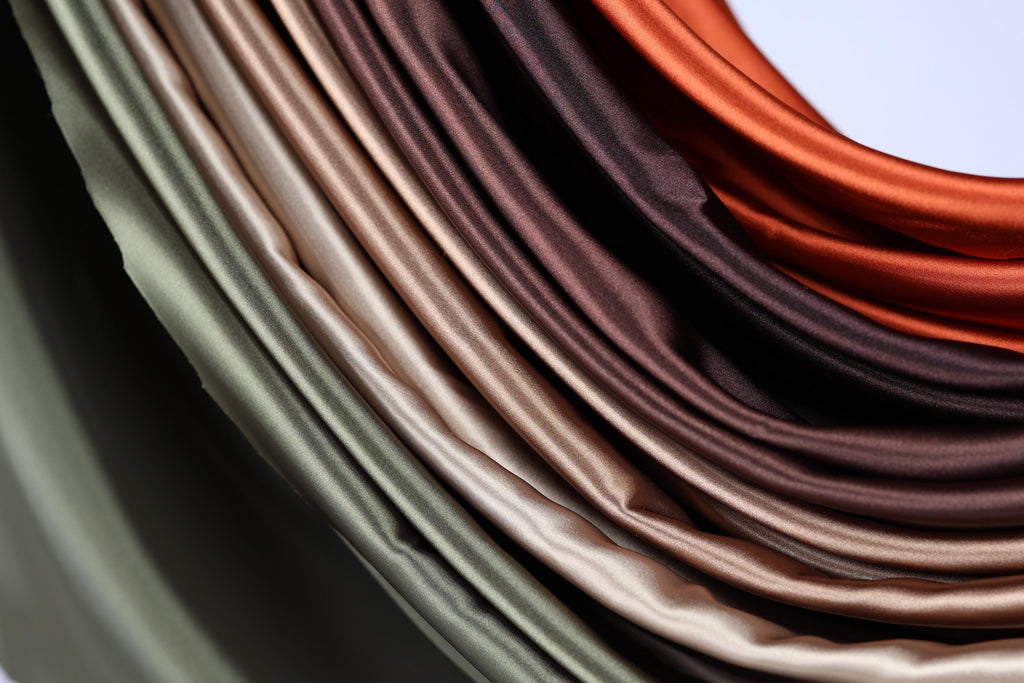 A close-up view of a pile of colorful satin fabric, with various shades of green, brown, and orange.