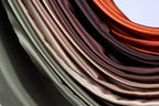 A close-up view of a pile of colorful satin fabric, with various shades of green, brown, and orange.