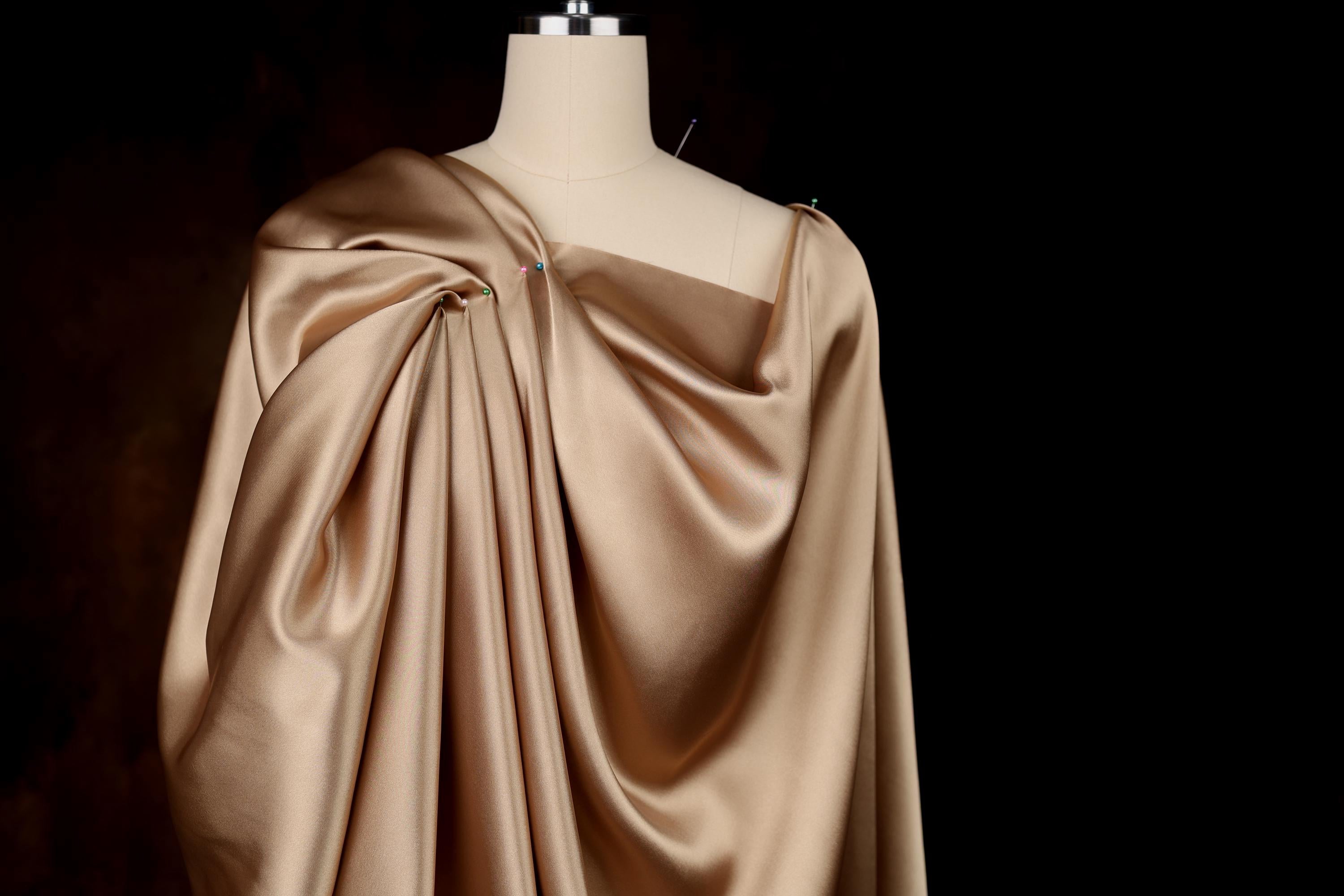 A mannequin wearing a beige satin dress with a draped, flowing silhouette.