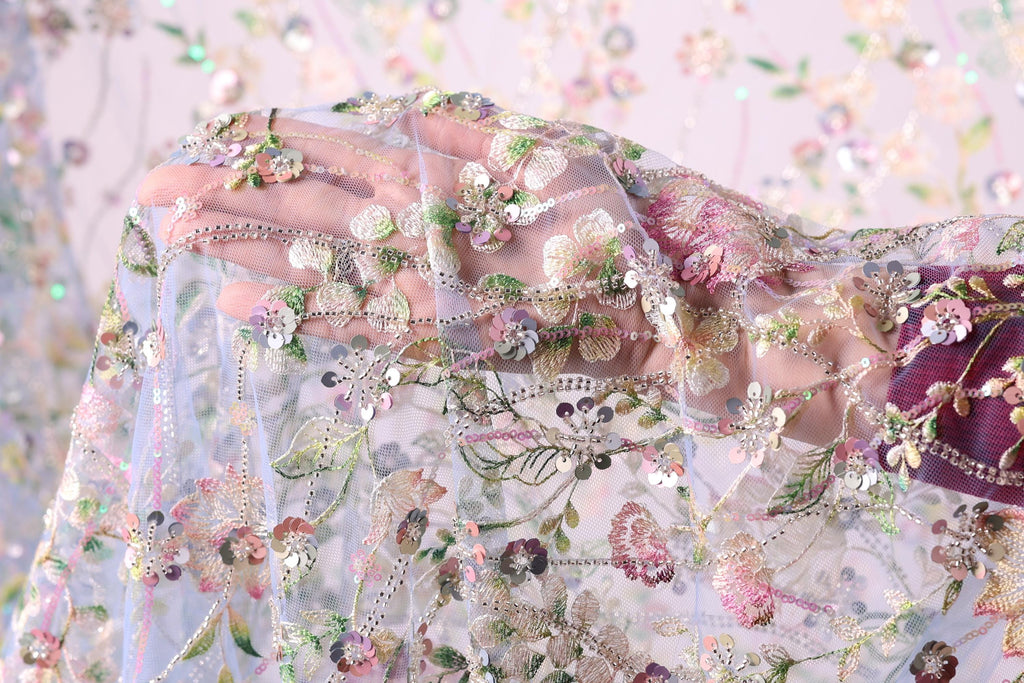 A close-up view of a hand holding a delicate, intricately embroidered fabric with a floral pattern.