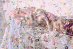 A close-up view of a hand holding a delicate, intricately embroidered fabric with a floral pattern.