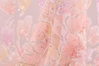 A close-up view of a delicate, pink fabric adorned with sparkling sequins and delicate floral patterns.