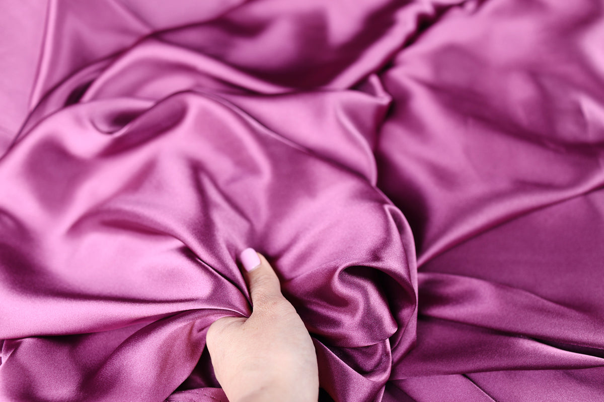 A hand is holding a piece of pink satin fabric, which appears to be soft and smooth.