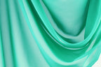 The image is a close-up of a turquoise fabric, with its folds and creases creating a textured and flowing appearance.
