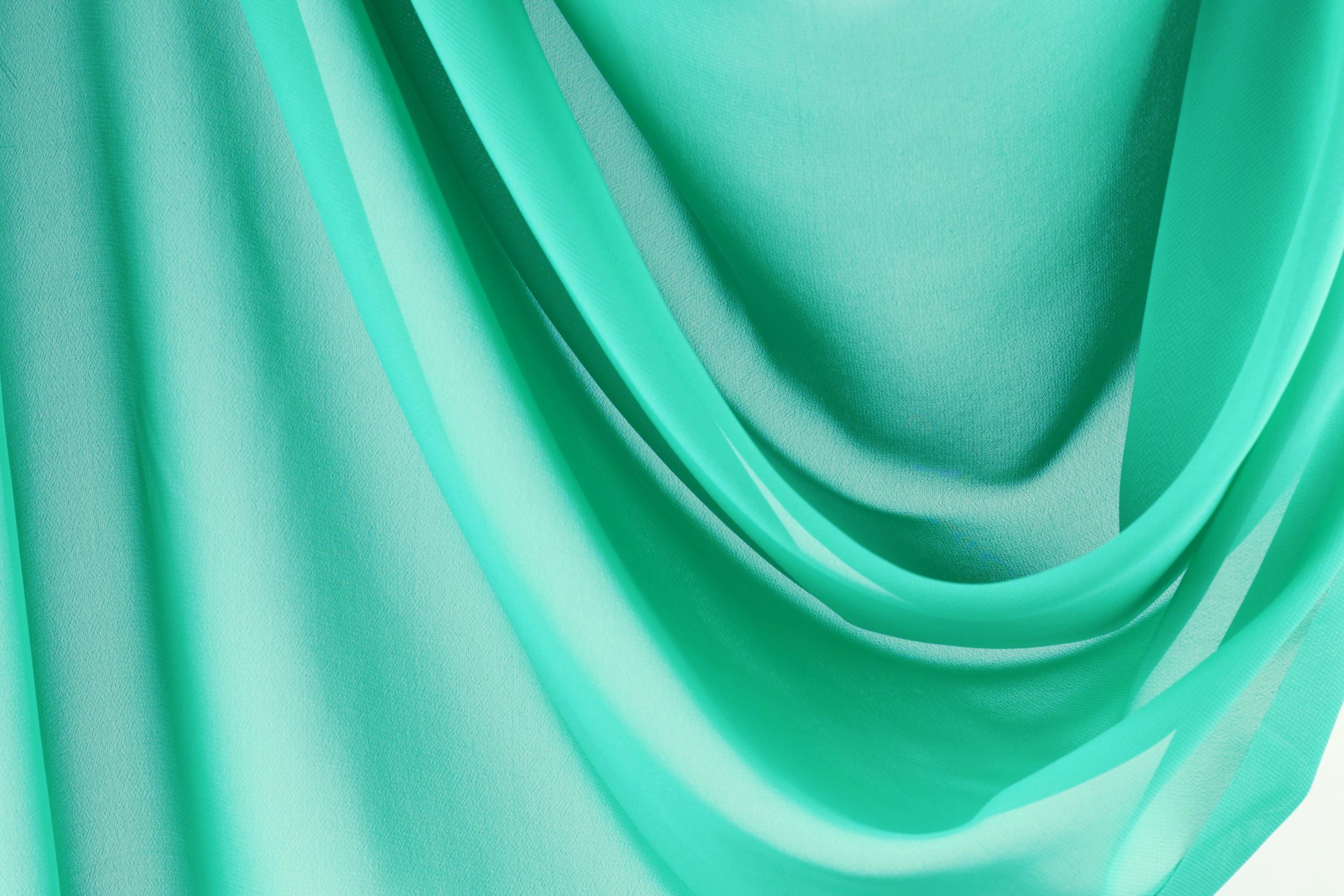 The image is a close-up of a turquoise fabric, with its folds and creases creating a textured and flowing appearance.