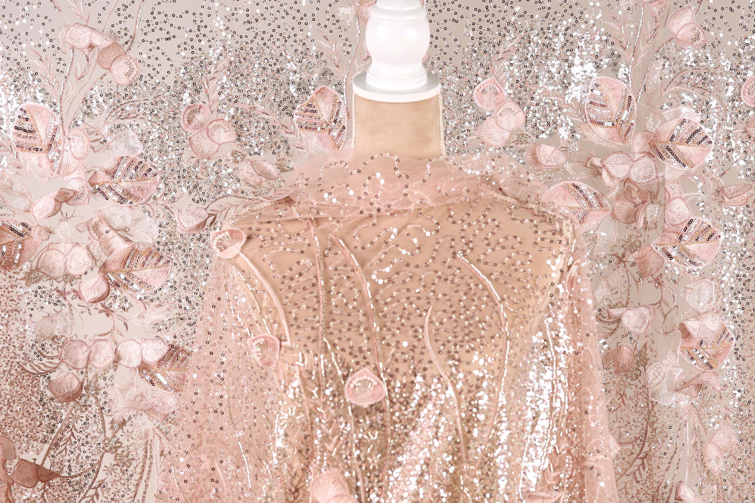 a pink sequin fabric with a floral pattern, displayed on a mannequin.