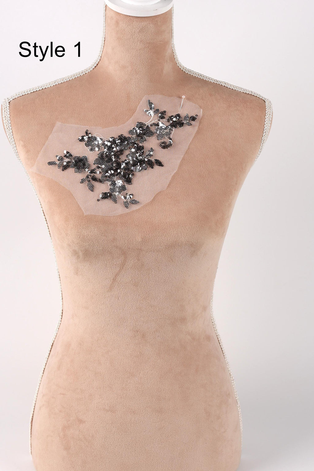 A mannequin with a beige body and a clear, transparent fabric patch on its chest, adorned with small black and silver beads.