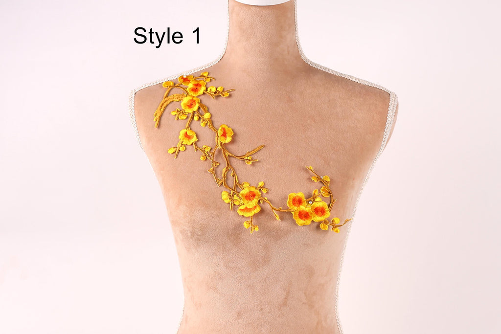 A mannequin with a decorative embroidered design on its shoulder, featuring yellow flowers and branches.