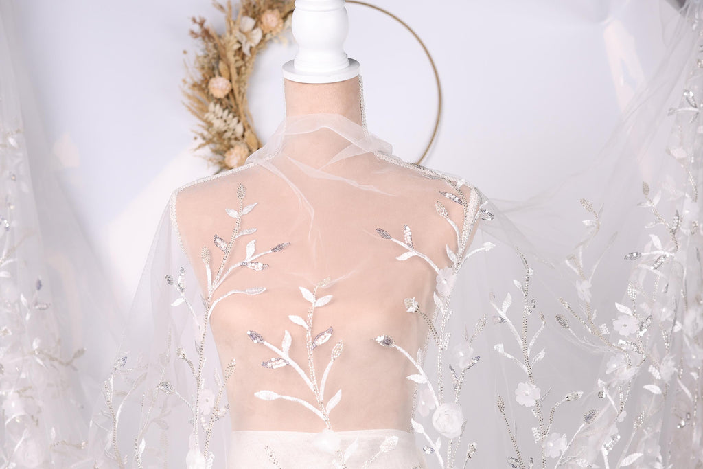 A mannequin wearing a white dress with a sheer, floral-patterned veil draped over it.
