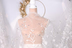 A mannequin wearing a white dress with a sheer, floral-patterned veil draped over it.
