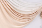 a close-up view of a fabric with a gradient of colors, transitioning from light to dark shades of peach and white. The fabric appears to be made of a soft, flowing material, possibly silk or chiffon, and is draped in a cascading manner, creating a sense of movement and elegance.