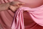 A hand is holding a pink fabric, possibly a piece of clothing, against a pink background.