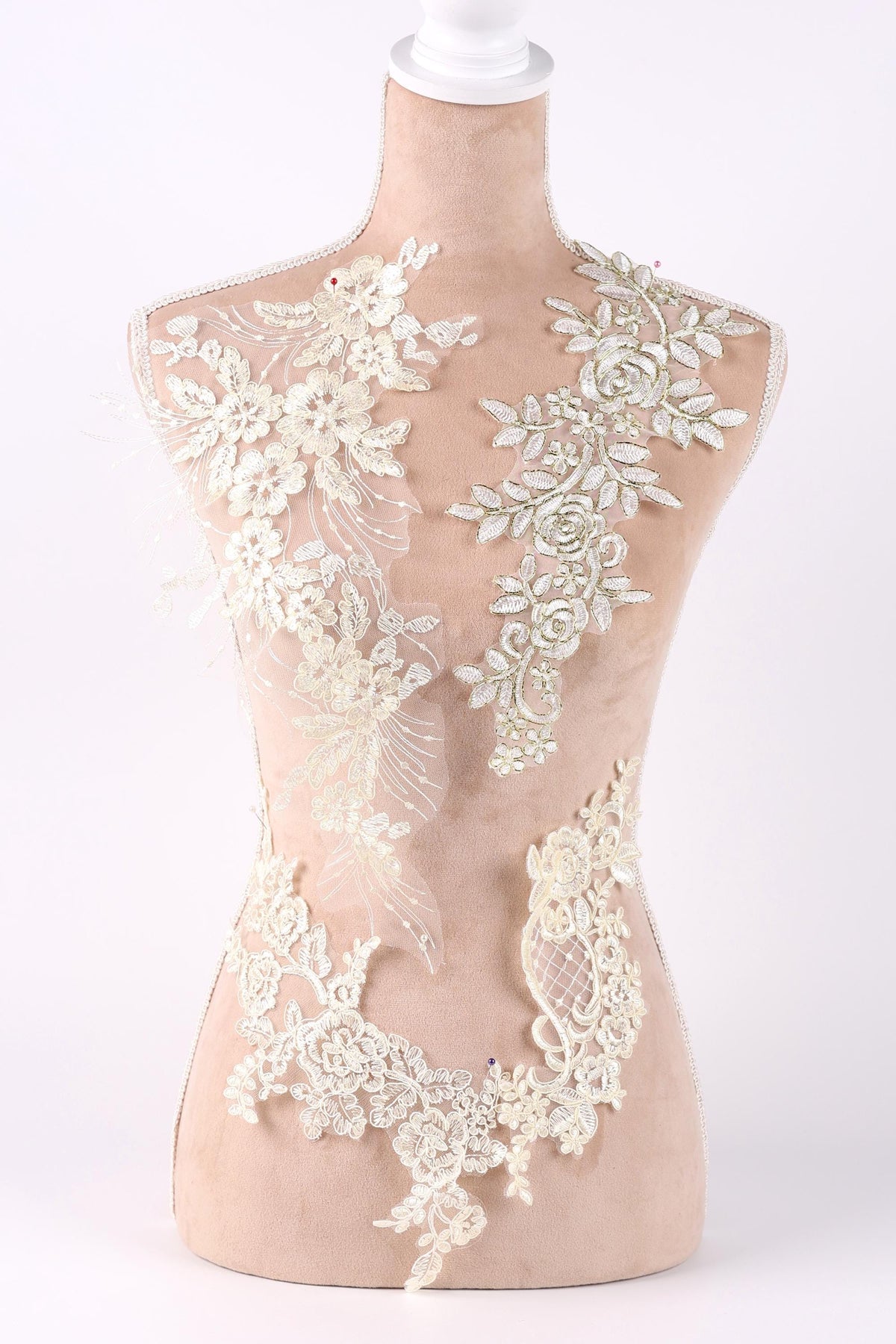 A mannequin with a beige body and white lace details on its torso, including floral and leaf-like patterns.