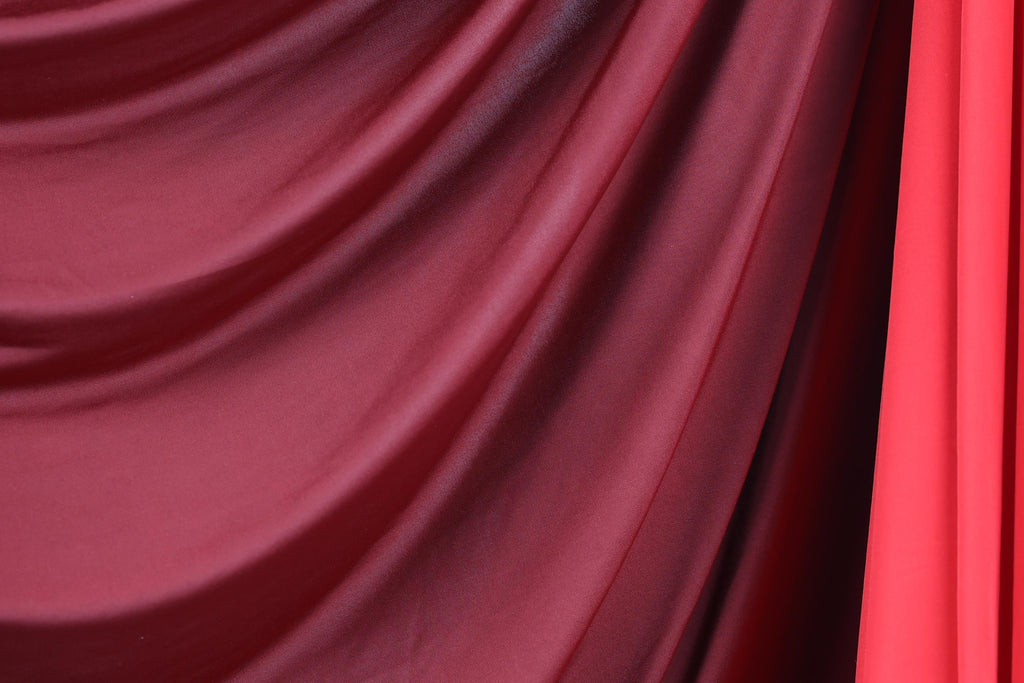 a close-up view of a red and maroon fabric, possibly a curtain or textile, with a slightly curled and draped appearance.