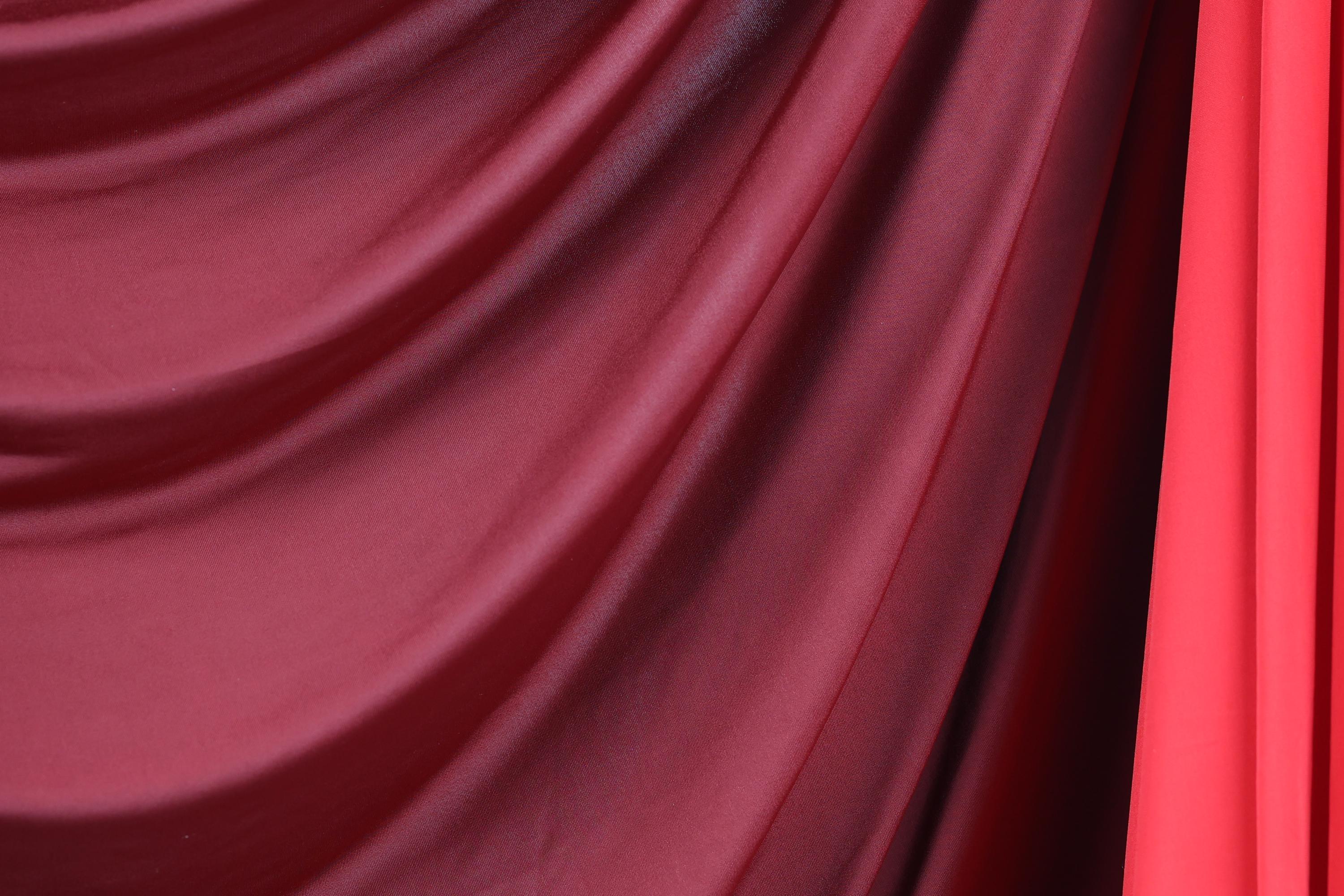 a close-up view of a red and maroon fabric, possibly a curtain or textile, with a slightly curled and draped appearance.