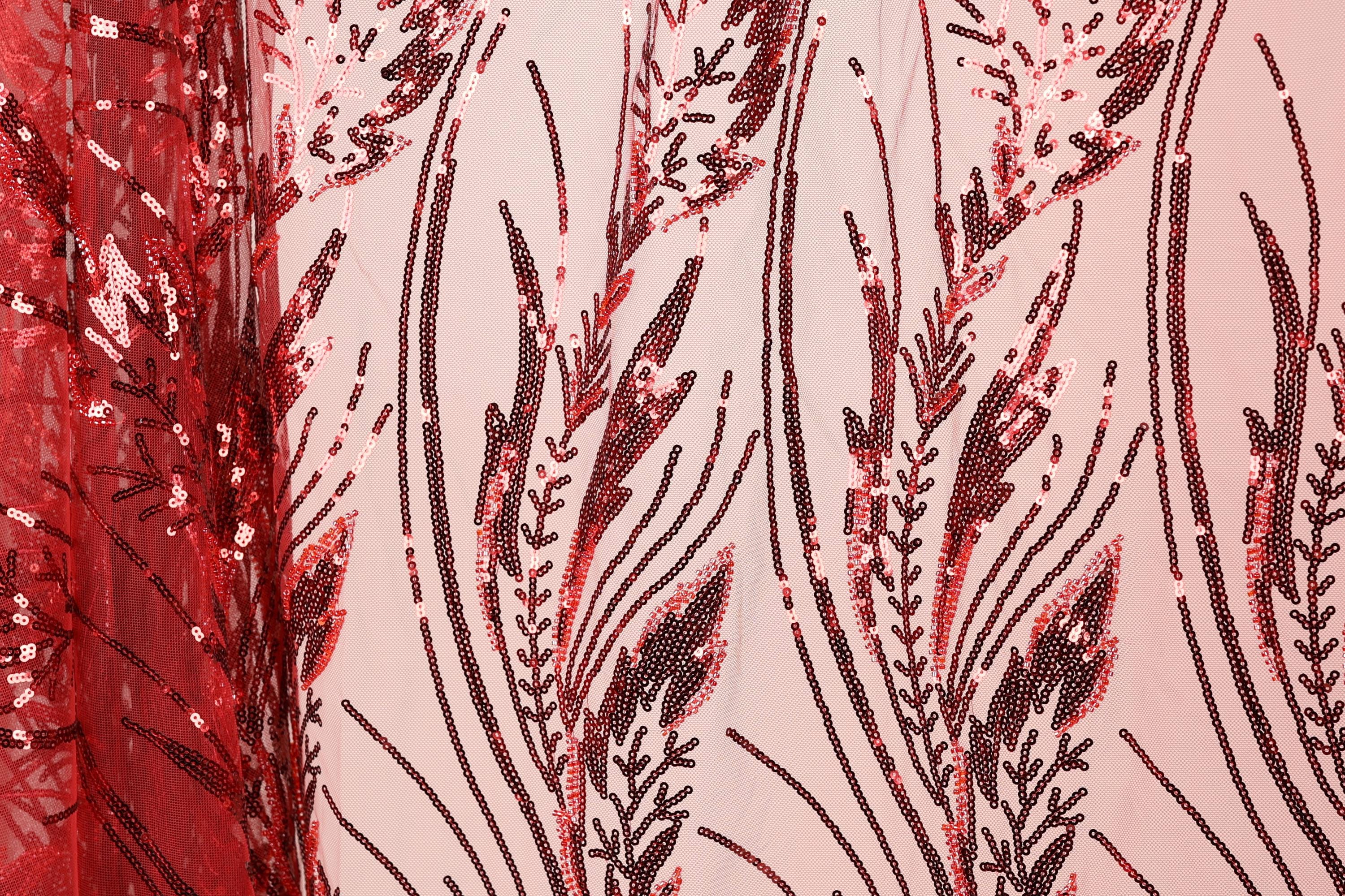 a close-up view of a fabric with a striking red and black sequin pattern. The pattern consists of various lines and shapes, creating a visually captivating design. The fabric appears to be a sheer material, allowing the intricate details of the sequin pattern to be clearly visible.