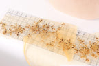 a close-up view of a ruler with a decorative gold and yellow floral pattern on it, placed on a white surface.