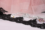 a pink tulle skirt, a black lace piece, a white measuring tape, and a small box of colorful pins.