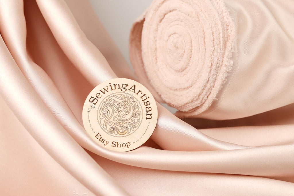 a close-up of a sewing artisan's logo on a piece of fabric, with a rolled-up fabric visible in the background.