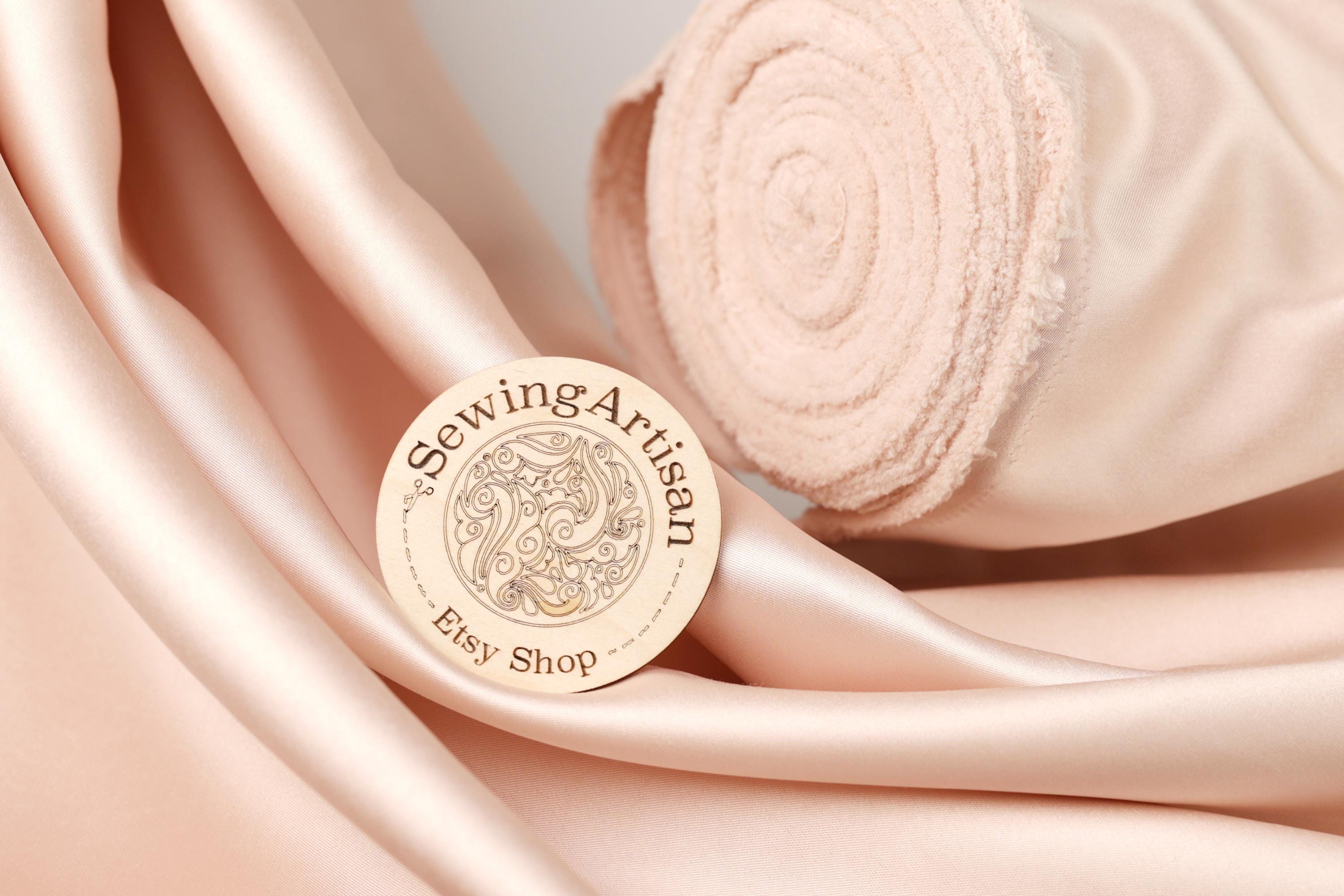 a close-up of a sewing artisan's logo on a piece of fabric, with a rolled-up fabric visible in the background.