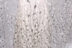 a close-up view of a delicate, white dress with a pattern of silver and white leaves or branches. The dress appears to be made of a sheer fabric, giving it a delicate and elegant appearance.